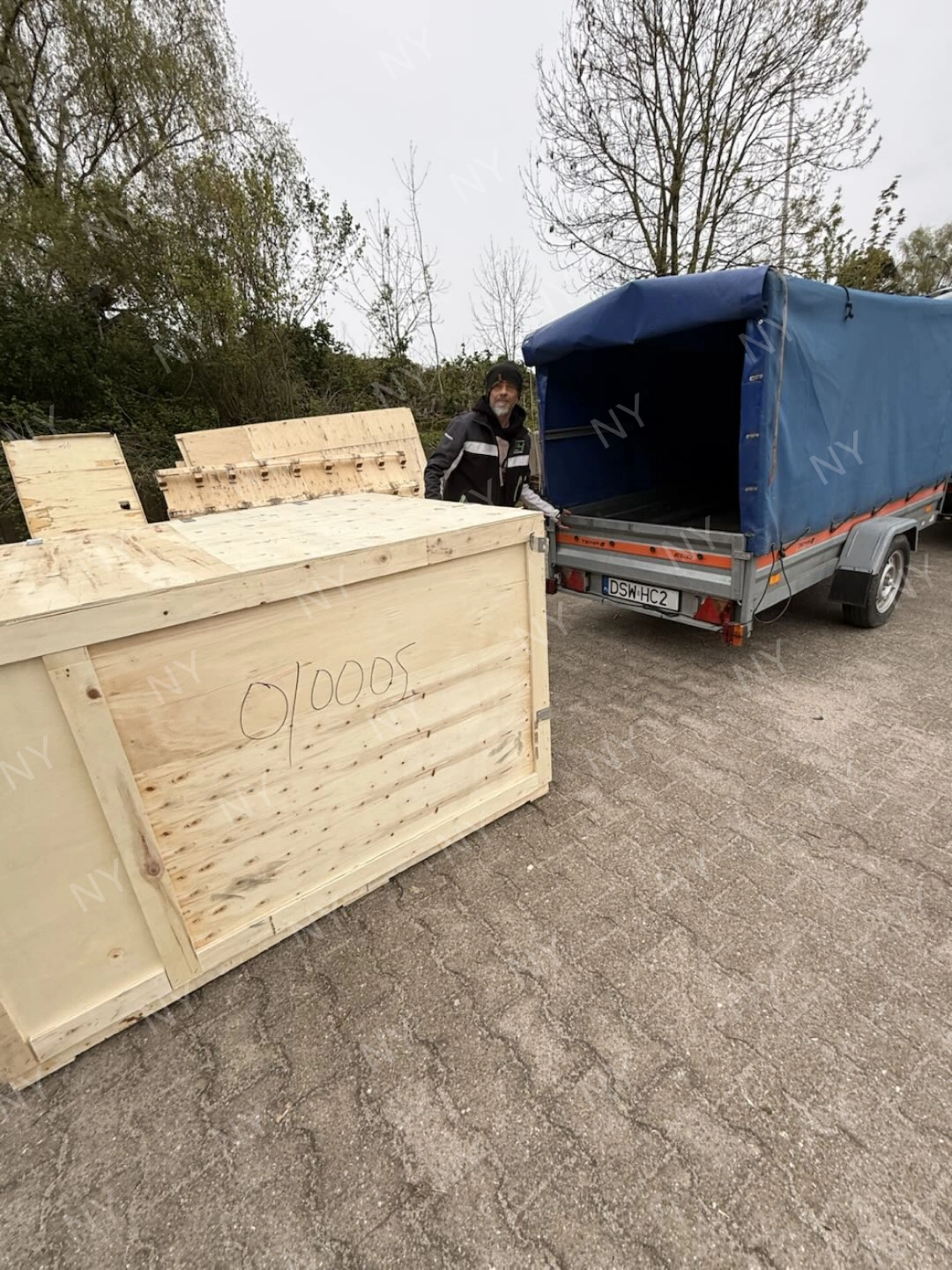 Customer opening delivered wooden crate beside transport trailer